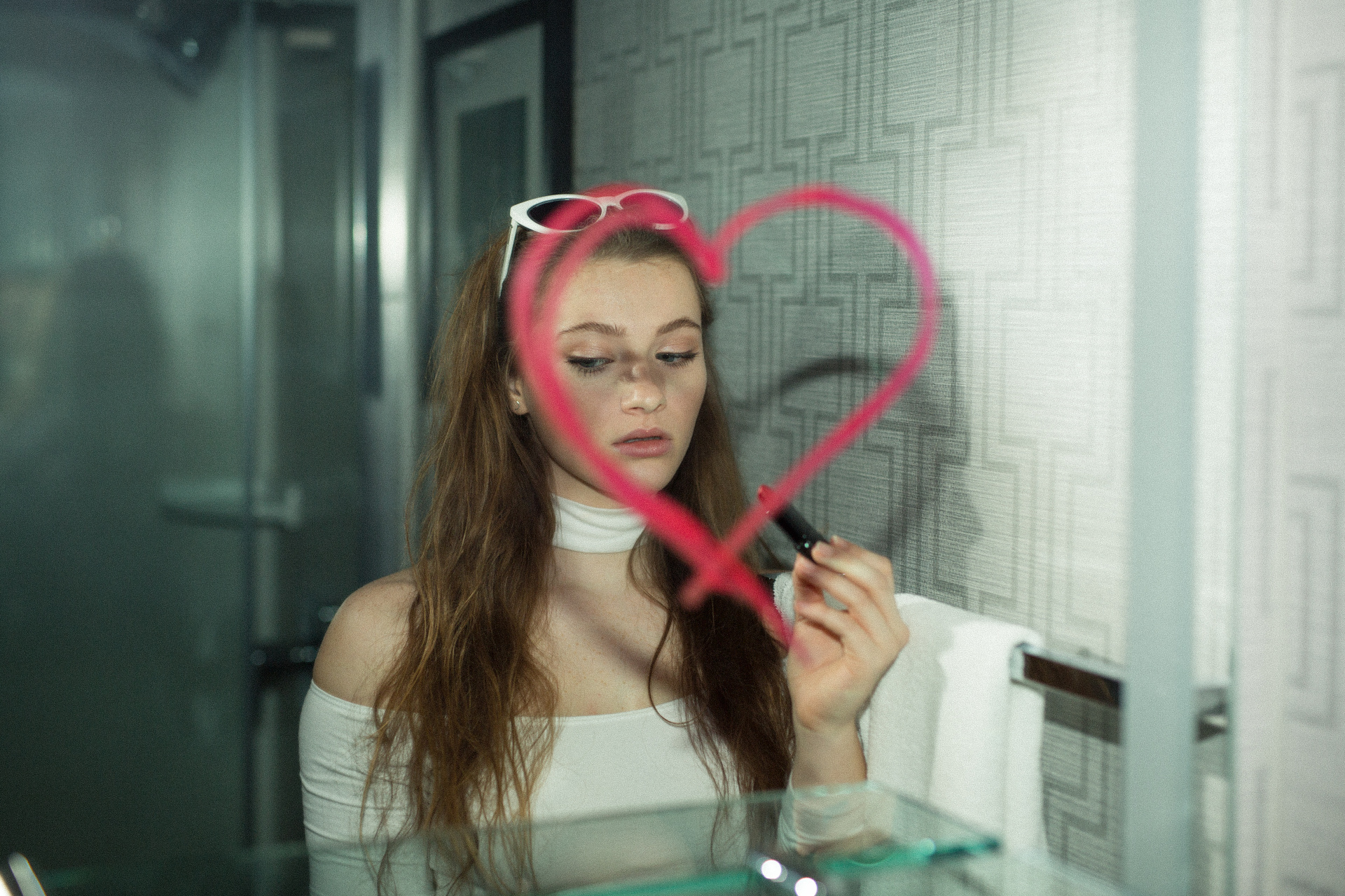 Woman looking into a mirror with a red heart drawn on it.